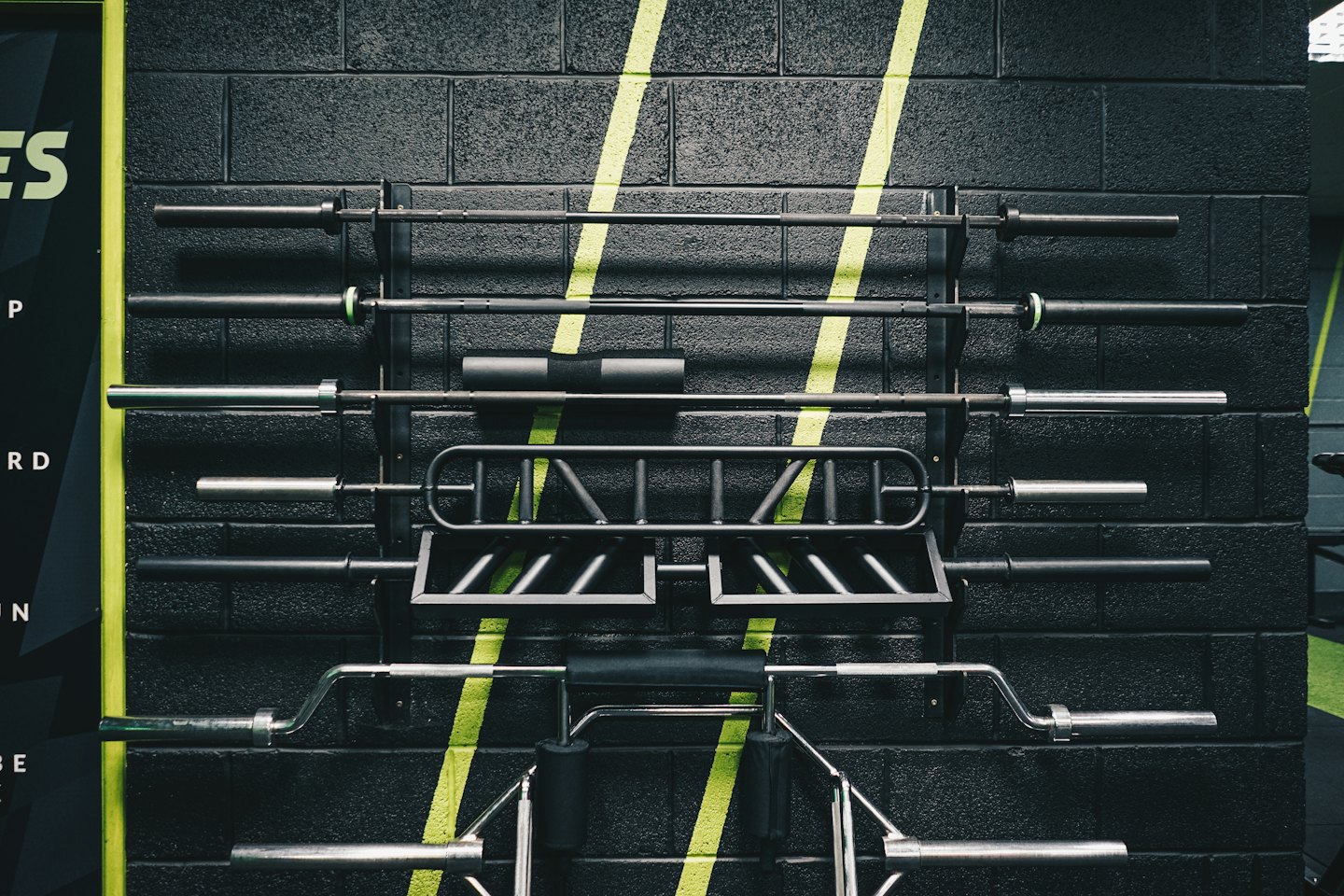 Metal weightlifting barbells and equipment on a gym wall rack.