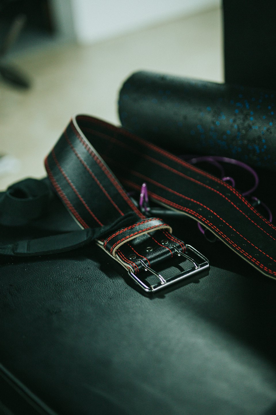 Black leather weightlifting belt with red stitching resting on a bench.