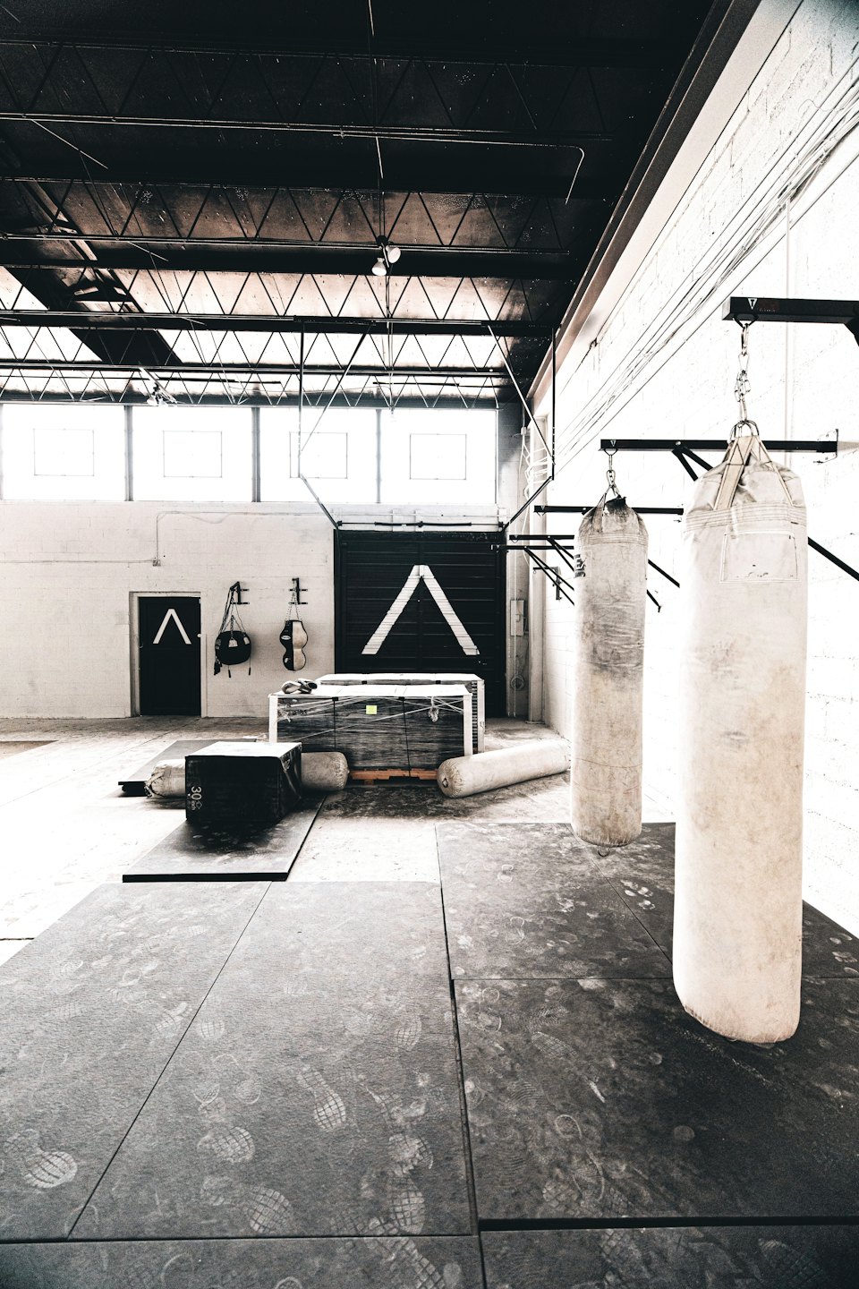 Industrial gym space with punching bags and scattered fitness equipment.