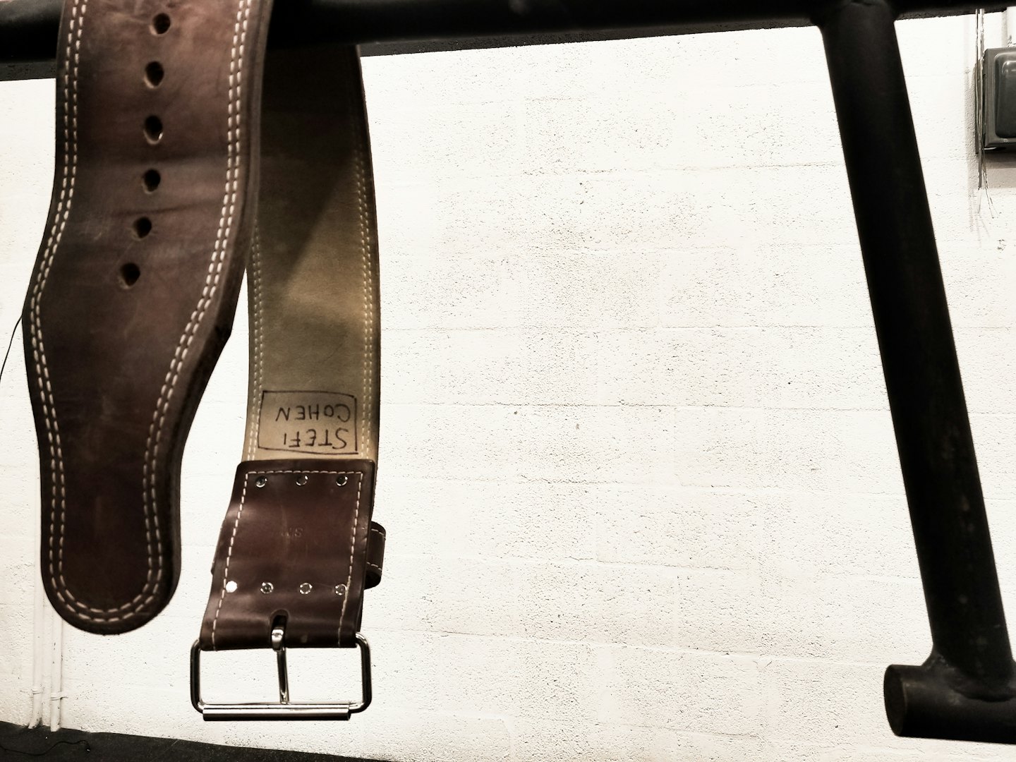 Leather weightlifting belt with metal buckle on a gym rack.