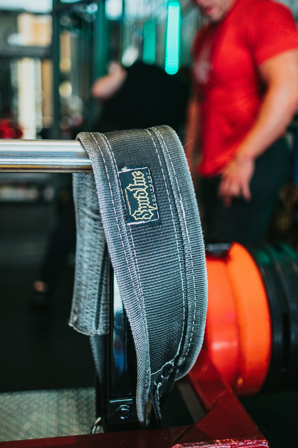 A weightlifting belt hangs over a chrome gym barbell.