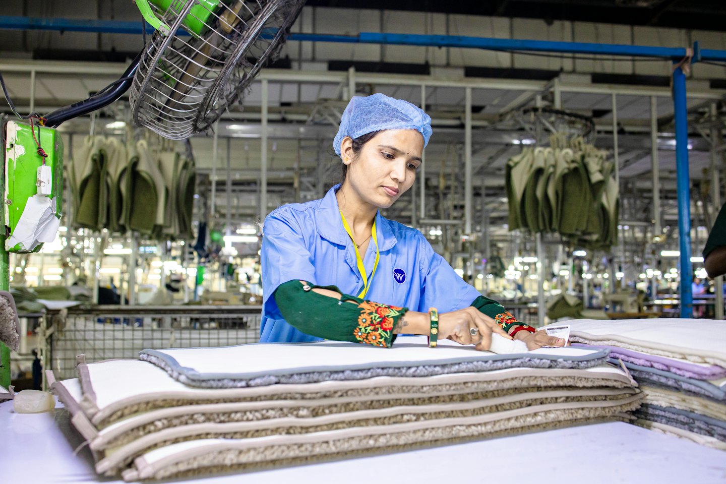 Factory worker inspecting stacks of textile products on a table.