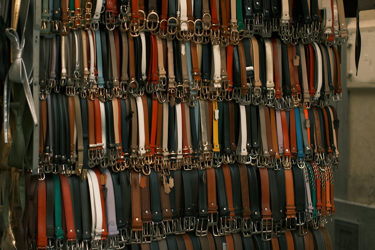 Leather belts hang in a row on a metal rack.