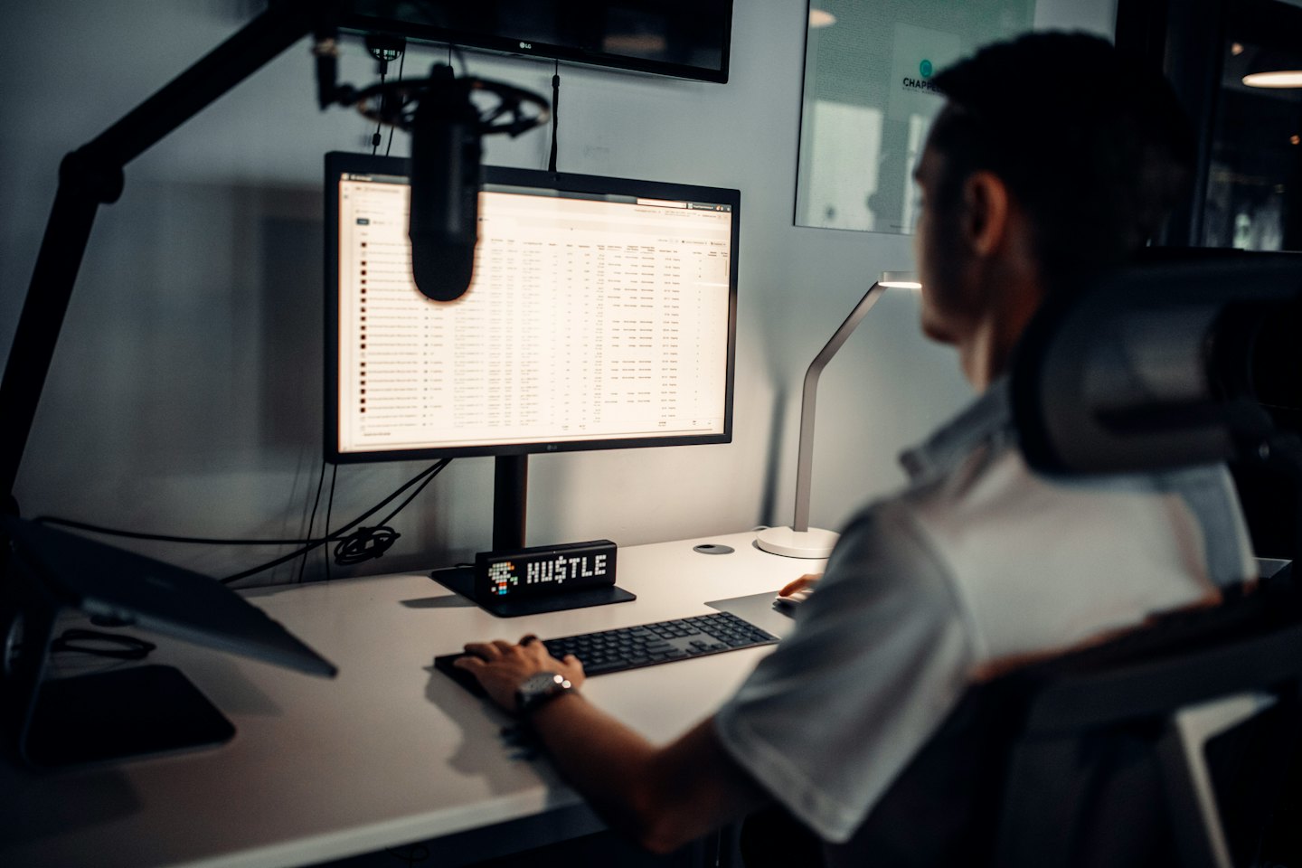 Person working on computer at office desk with 'HUSTLE' sign.